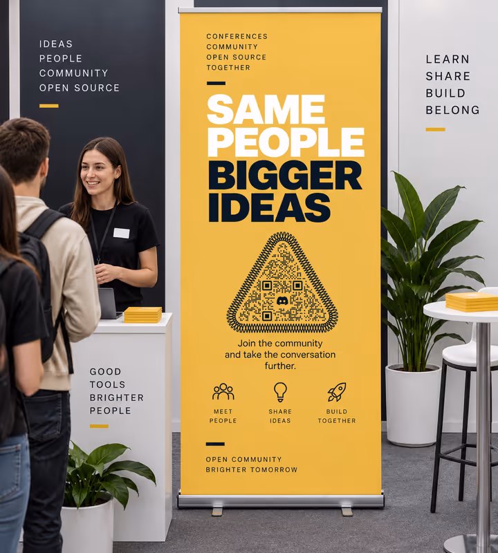 A yellow roll-up banner reading “Same people, bigger ideas” with a black triangular QR code, on an open-source conference stand where two people are talking