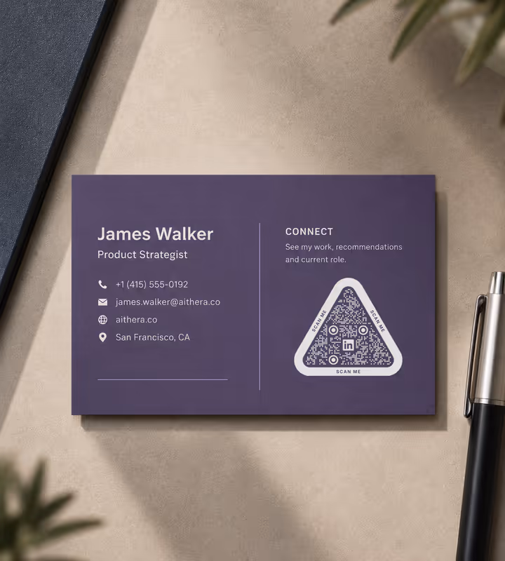 A purple business card with contact details and a rounded triangular QR code marked “Scan me”, lying on stone beside a pen