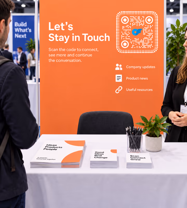 An orange expo backdrop reading “Let's stay in touch” with a white rounded QR code, above a stand table stacked with printed booklets