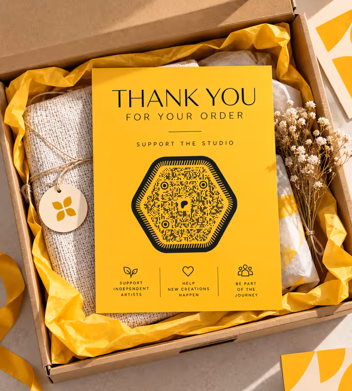 A yellow “Thank You for Your Order” card with a dark hexagonal QR code, tucked into a parcel among yellow tissue paper, knitwear and dried flowers
