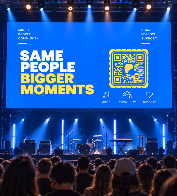 A large blue stage screen reading “Same people, bigger moments” with a yellow square QR code, above a crowd at a live gig