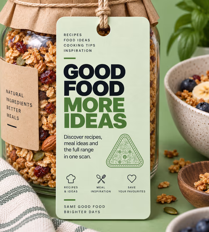 A green “Good food, more ideas” tag with a triangular QR code, tied to a granola jar beside a bowl of yoghurt and fruit