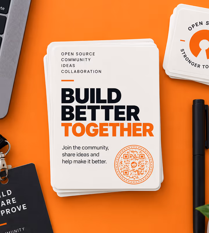 A stack of white “Build better together” stickers with an orange circular QR code, on an orange desk beside a laptop and a pen