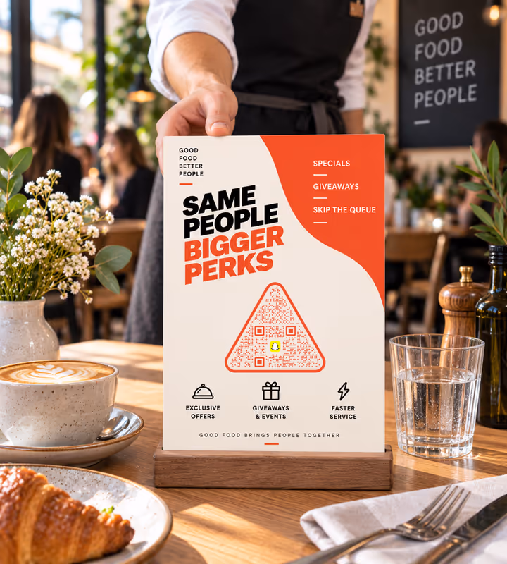 A cafe table card reading “Same people, bigger perks” with an orange triangular QR code, handed over by a member of staff in an apron