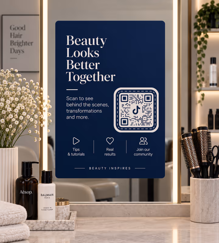 A navy panel reading “Beauty looks better together” with a white square QR code, mounted on a lit salon mirror above styling products