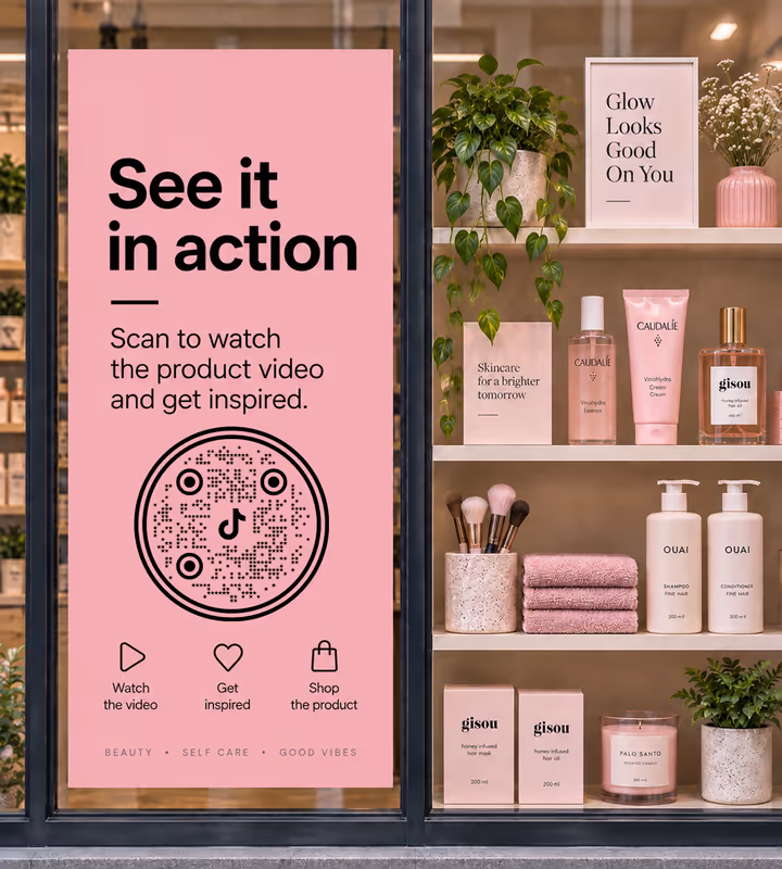 A pink window poster reading “See it in action - scan to watch the product video” with a black circular QR code, beauty products on the shelves behind