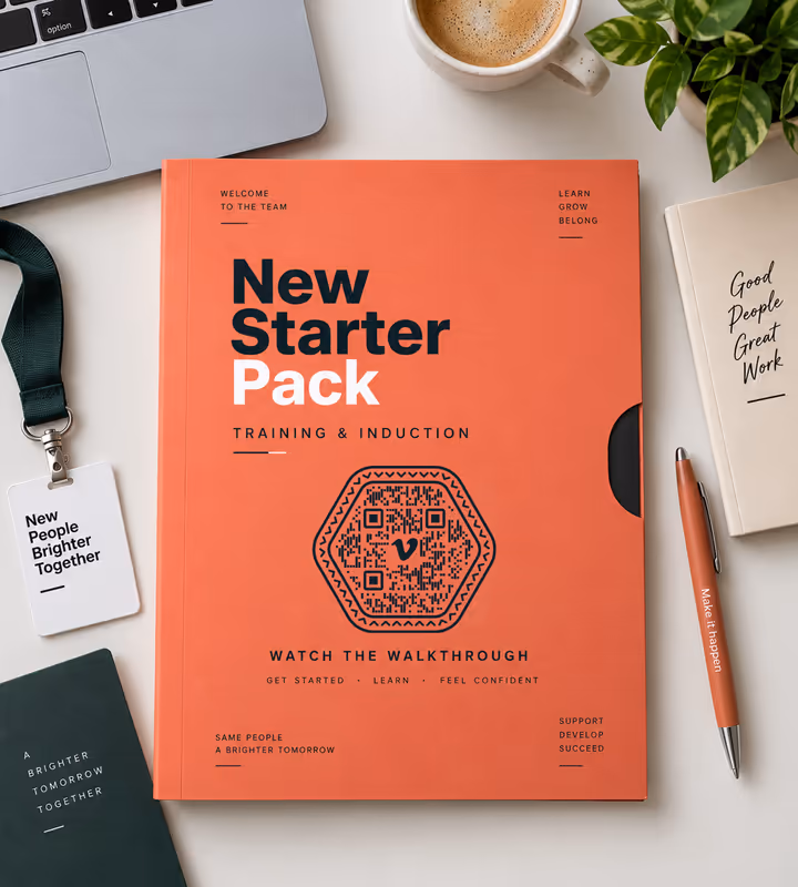 An orange “New starter pack - training and induction” folder with a hexagonal QR code and “Watch the walkthrough”, on a desk with a lanyard and coffee