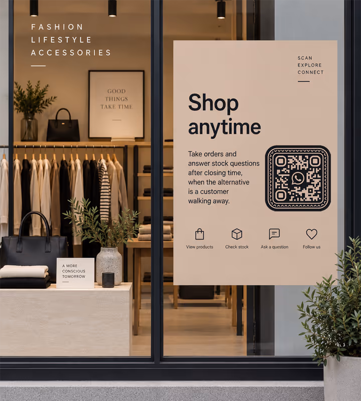 A cream “Shop anytime” window poster with a black rounded QR code, in the window of a fashion shop with clothing rails behind the glass