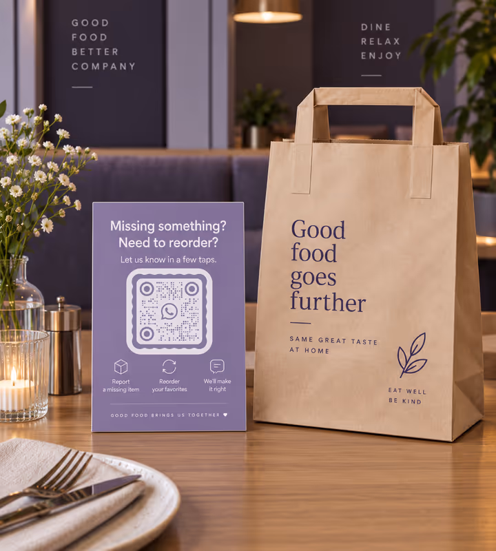 A purple table card asking “Missing something? Need to reorder?” with a square QR code, standing beside a paper takeaway bag