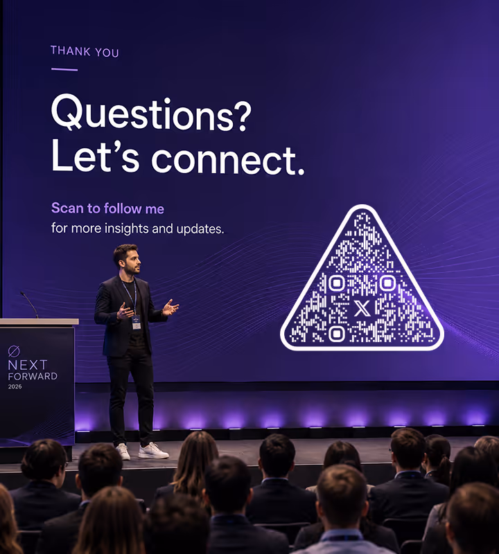 A purple stage screen reading “Questions? Let's connect - scan to follow me” with a white triangular QR code, a speaker on stage before a seated audience