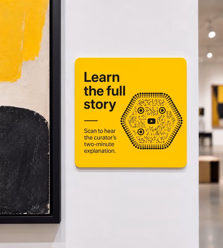 A yellow gallery wall panel reading “Learn the full story - scan to hear the curator's two-minute explanation” with a black hexagonal dotted QR code, beside a painting