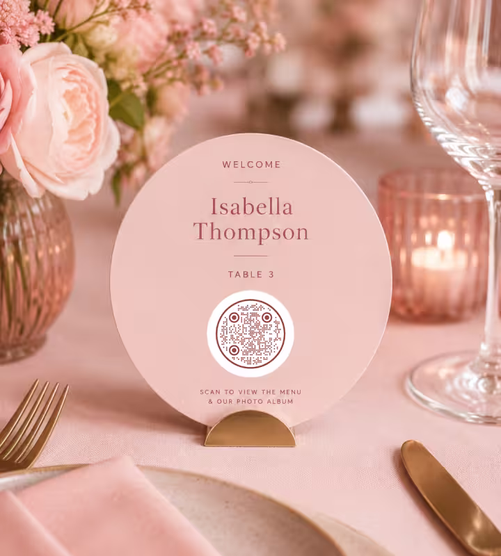 A round blush wedding place card for Isabella Thompson, Table 3, with a circular QR code to view the menu and photo album