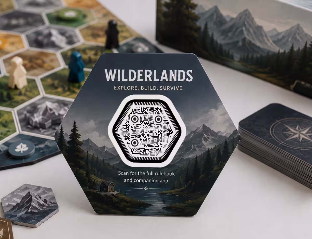 กล่องบอร์ดเกมทรงหกเหลี่ยม "Wilderlands" ที่มีภาพภูเขาและ QR Code หกเหลี่ยม ข้าง ๆ มีชิ้นส่วนเกม
