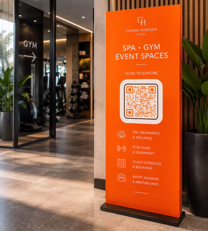 ป้ายผ้าสีส้มของโรงแรมที่เขียนว่า "Spa · Gym · Event Spaces" พร้อม QR Code ตั้งอยู่ข้างทางเข้าฟิตเนส