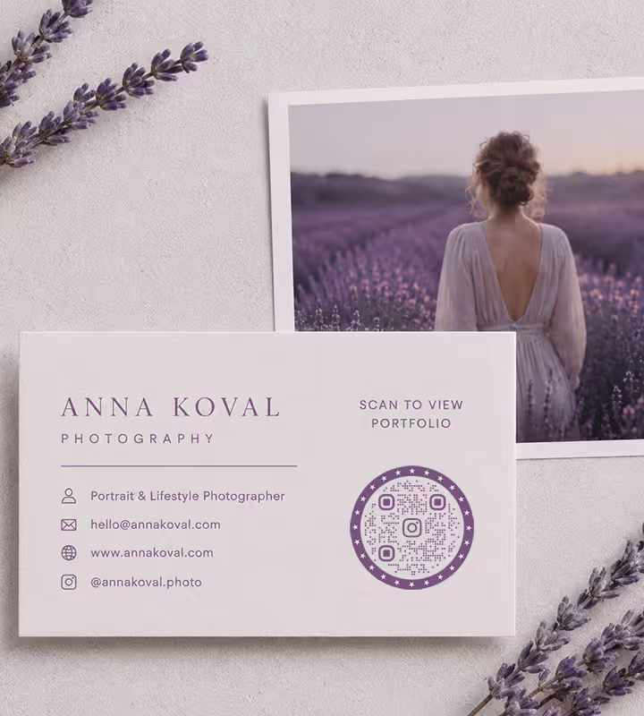 A photographer's business card with a circular purple QR code, laid on stone beside a lavender portrait print