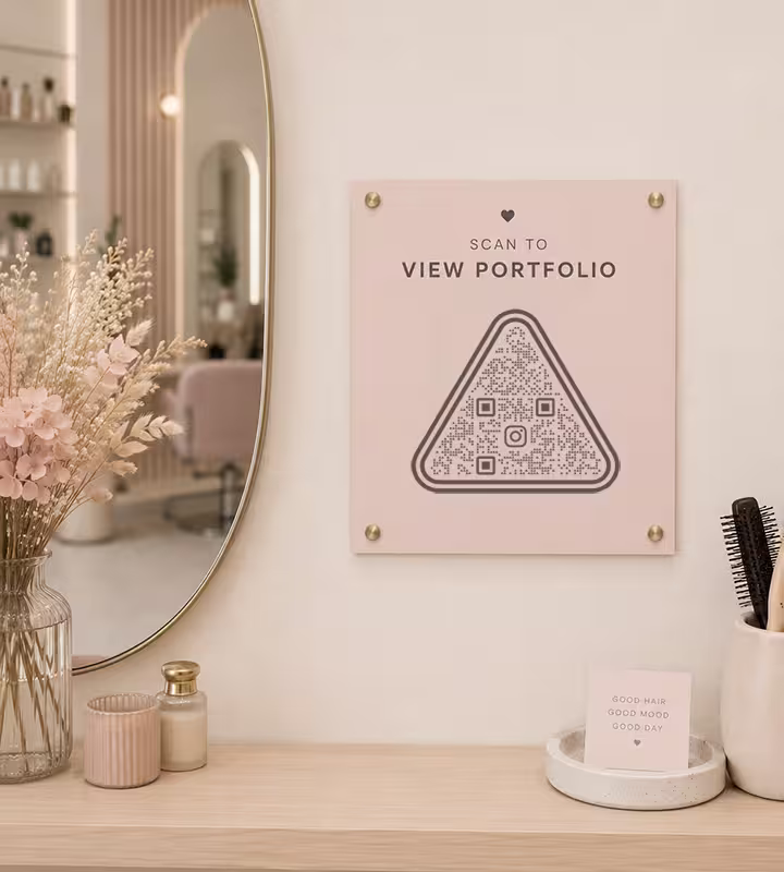 A pink “Scan to view portfolio” panel with a triangular QR code, on a salon wall beside a round mirror
