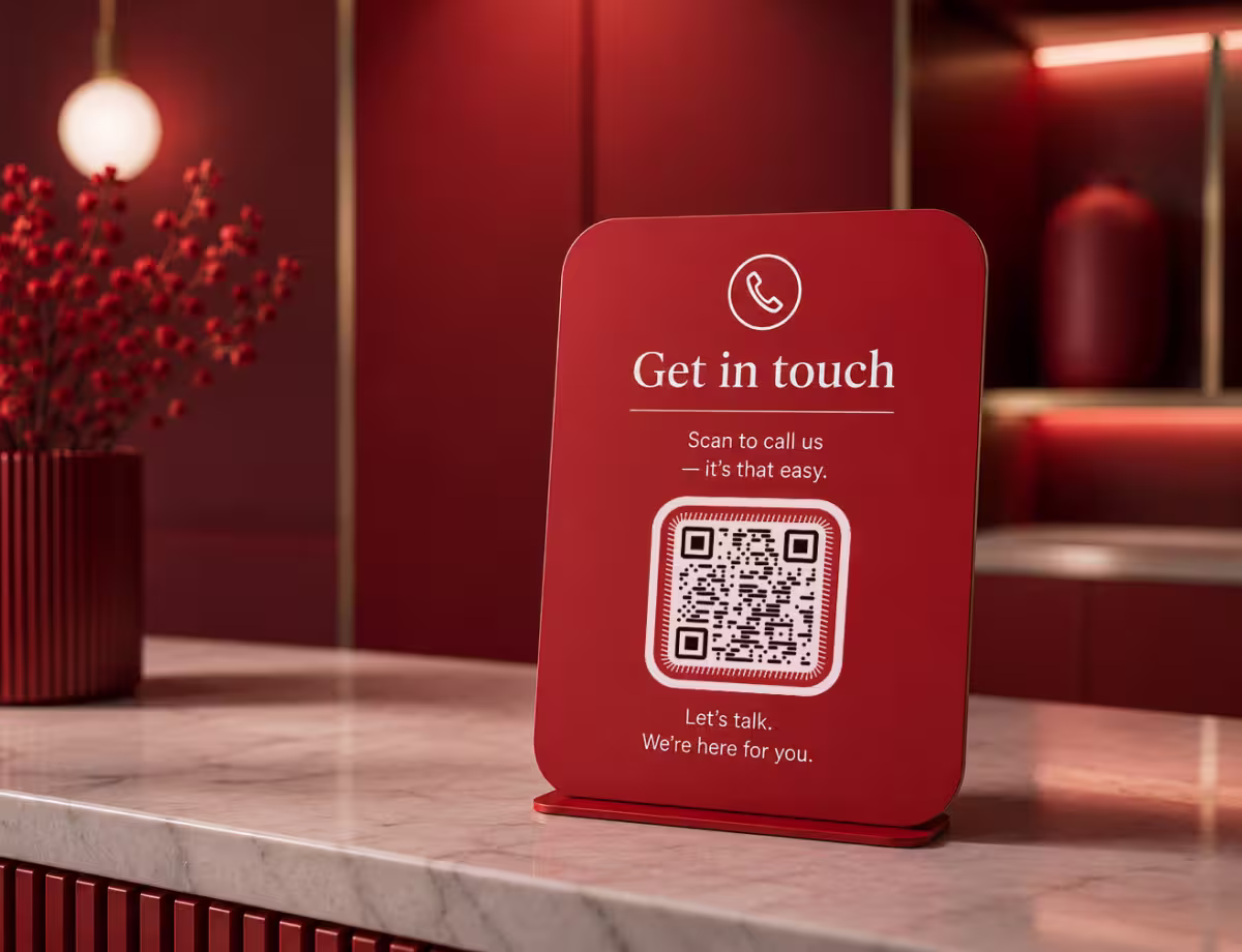 ป้ายที่เคาน์เตอร์สีแดง ข้อความ "ติดต่อเรา - สแกนเพื่อโทรหาเรา" พร้อม QR Code ตั้งอยู่บนเคาน์เตอร์หินอ่อนข้างแจกันสีแดง