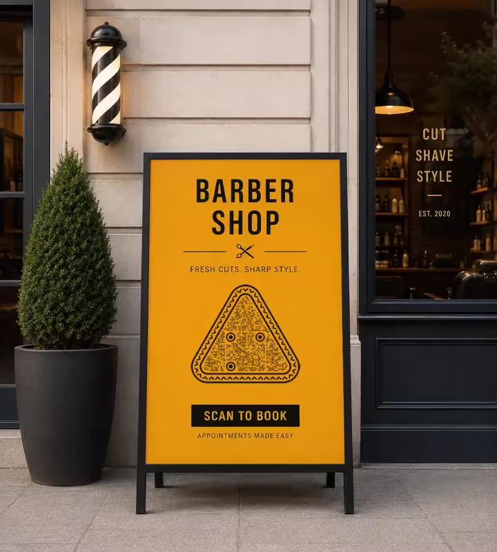 A yellow pavement A-board outside a barbershop with a triangular QR code and “Scan to book - appointments made easy”, beside the barber pole