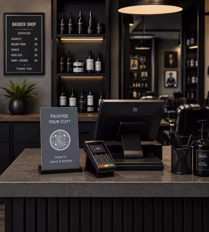 A counter sign at a barbershop till reading “Enjoyed your cut? Scan to leave a review”, standing beside the card machine
