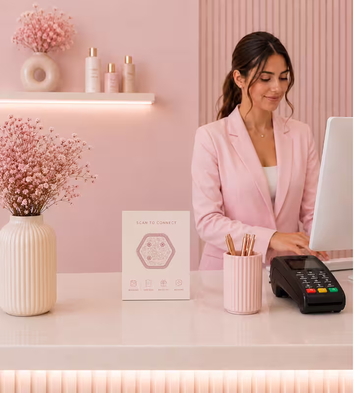 A card on a pink salon reception desk reading “Scan to connect”, with a hexagonal QR code and icons for booking, offers, social and reviews, beside the card machine
