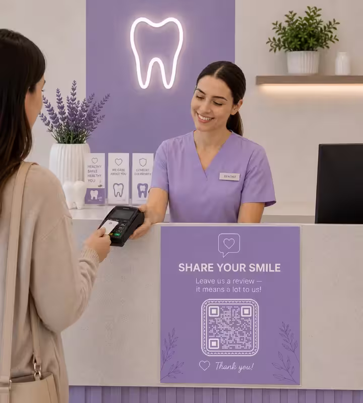 Uma paciente pagando com cartão na recepção de uma clínica odontológica, com um painel roxo no balcão dizendo «Compartilhe o seu sorriso: deixe uma avaliação» acima de um QR code quadrado