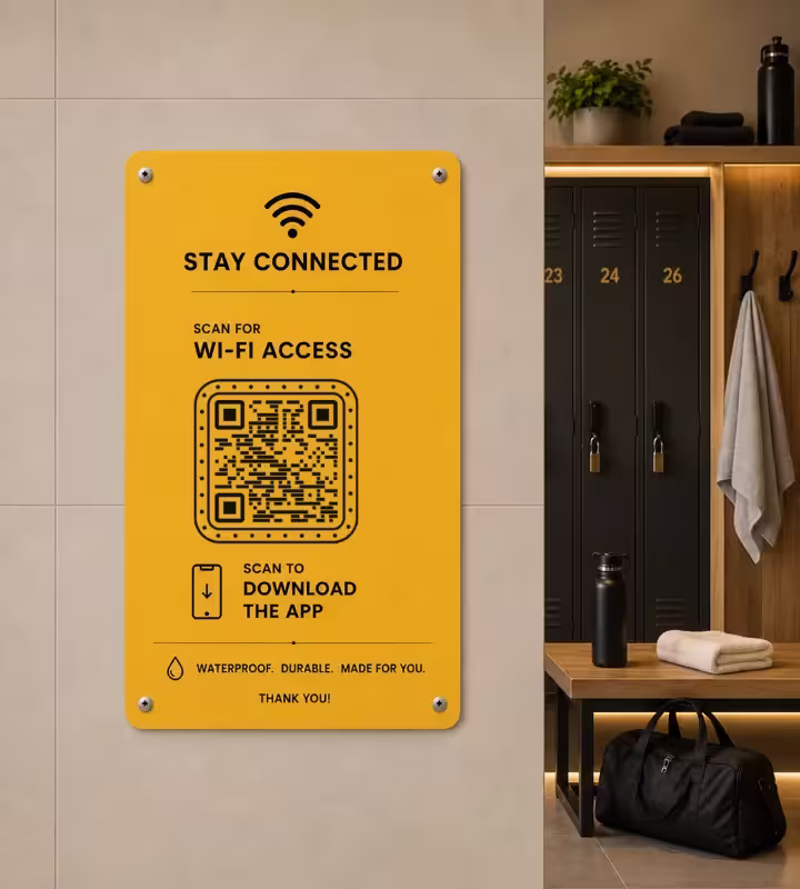टाइल वाली लॉकर रूम की दीवार पर लगा पीला साइन, जिस पर “Stay connected - scan for Wi-Fi access”, QR कोड और सदस्यों को ऐप डाउनलोड करने का न्योता है, पीछे लॉकर और बेंच
