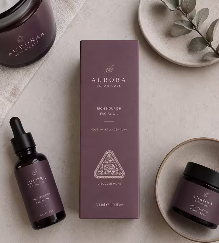 A plum facial oil carton with a triangular QR code marked “Discover more” on the front, beside the dropper bottle and a jar of cream