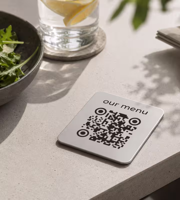 A small QR code sign on a restaurant table labeled “our menu” beside a glass of water