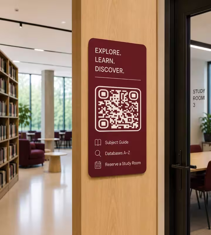 Um painel bordô em um pilar de madeira ao lado da porta de uma sala de estudos, com «Explore. Aprenda. Descubra.», um QR code quadrado e os itens guia por área, bases de dados A-Z e reservar sala de estudos; atrás, as estantes da biblioteca