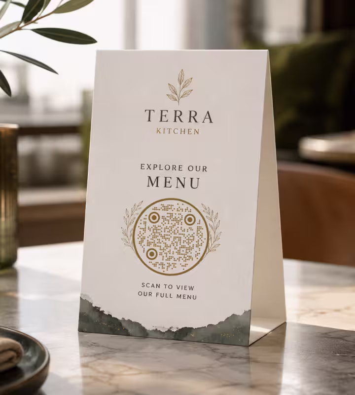A “Terra Kitchen - explore our menu” folded table card with a round QR code, standing on a marble table