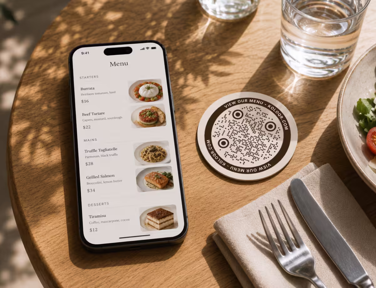 A round brown “View Our Menu” drinks coaster with a circular QR code on a wooden table, beside a phone showing the menu