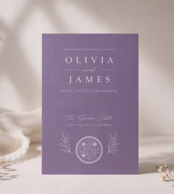A purple “Olivia and James” wedding invitation with a delicate round QR code at the bottom, on soft white fabric