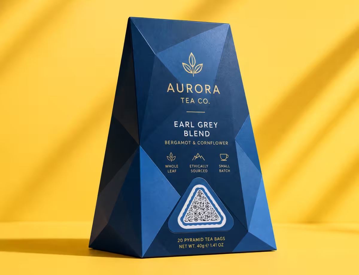 ซองชาสีน้ำเงินแบบเหลี่ยมเจียระไน "Aurora Tea Co - Earl Grey Blend" บนพื้นหลังสีเหลือง พร้อม QR Code ทรงสามเหลี่ยม