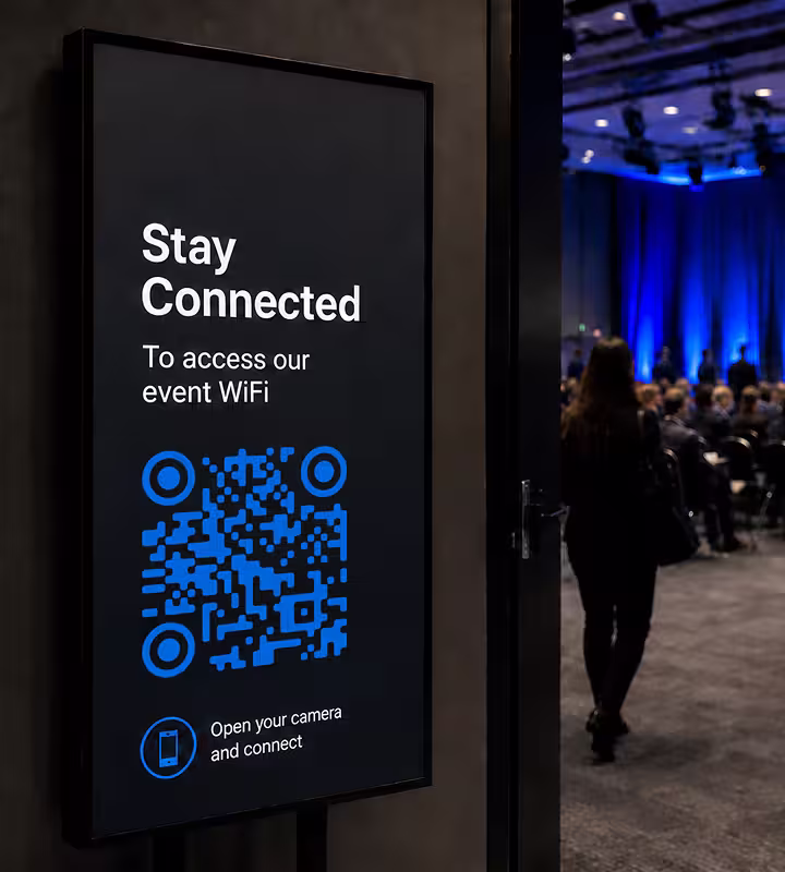 A digital standing sign at an event reading “Stay Connected - to access our event WiFi” above a QR code
