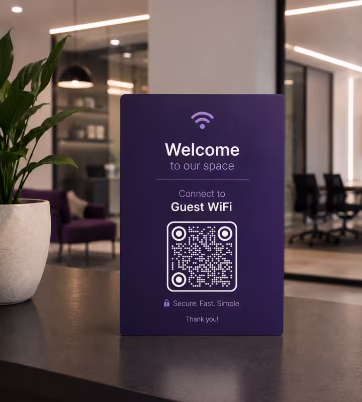 A purple “Welcome to our space - connect to Guest WiFi” standing sign on a desk in an office lounge